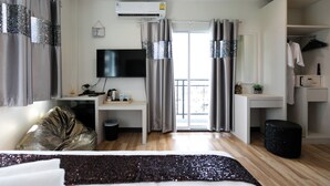 A modern hotel room with a bed, a desk with a flat-screen TV, a wardrobe, and a small balcony.