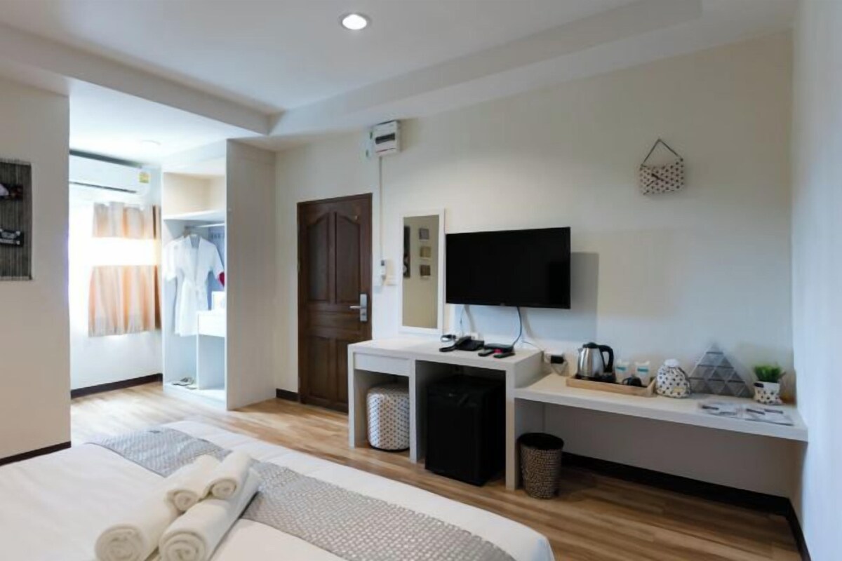 Ein modernes Hotelzimmer mit einem Bett, einem Schreibtisch mit Computer, einem Fernseher und einer kleinen Küchenzeile.