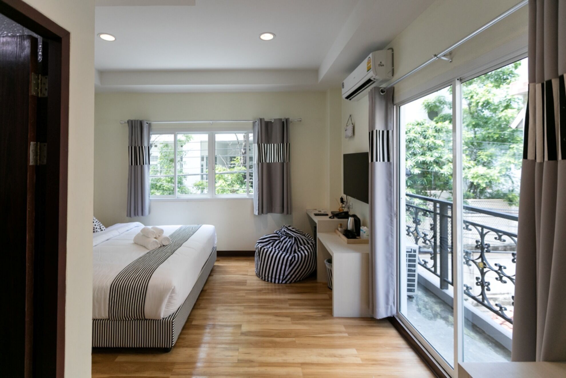A hotel room with a bed, a desk, a TV, and a balcony with a railing.