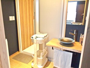 A compact bathroom with a sink, a mirror, a towel rack, and a small basket with towels. - Shounsai (Kyoto)