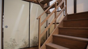 A wooden staircase with a handrail leading to a room with sliding doors featuring a nature scene. - Shounsai (Kyoto)