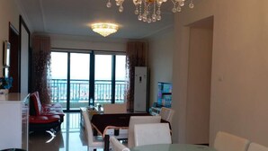 A spacious living room with a large dining table, white chairs, a chandelier, and a view of the city through large windows. - Henda Venice Hotel (Nantong)