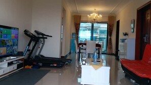 A spacious living area with a treadmill, a flat-screen TV, a coffee table, and a red sofa. - Henda Venice Hotel (Nantong)
