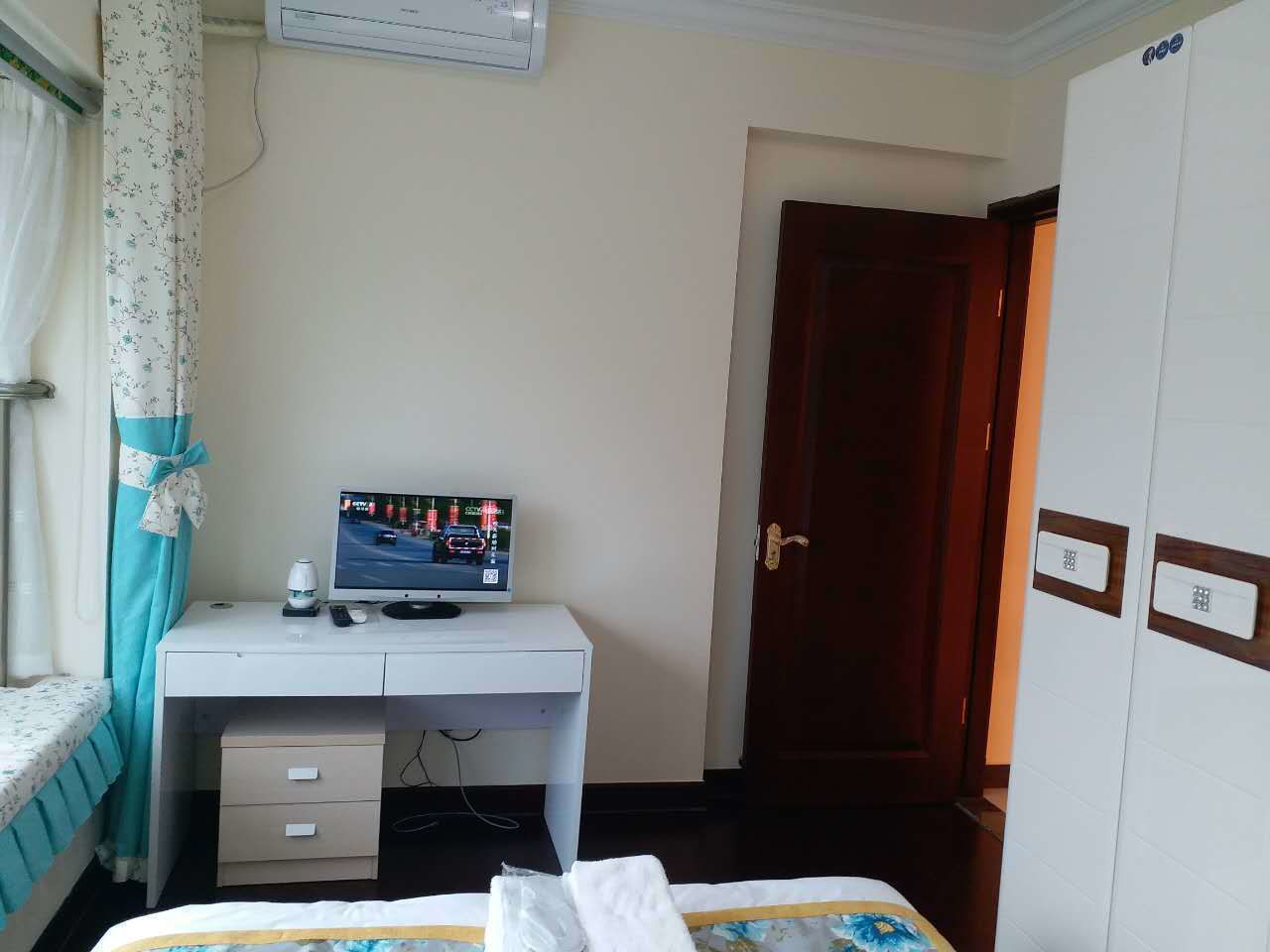 A hotel room with a desk, a bed, an air conditioning unit, and a wardrobe.