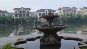 A fountain in a courtyard with a reflection in the water, surrounded by buildings with a consistent architectural style. - Henda Venice Hotel (Nantong)