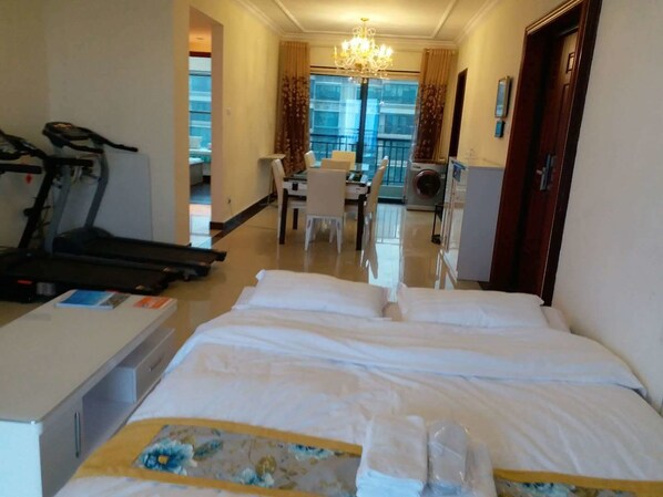 Habitación de hotel con cama, cinta de correr, escritorio y zona de comedor.