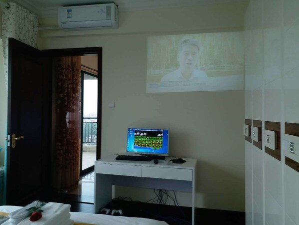 A room with a bed, a desk with a computer, a projector on the wall, and a door. - Henda Venice Hotel (Nantong)