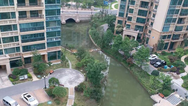 A riverside residential area with modern buildings, a pedestrian bridge, and a small park with benches. - Henda Venice Hotel (Nantong)