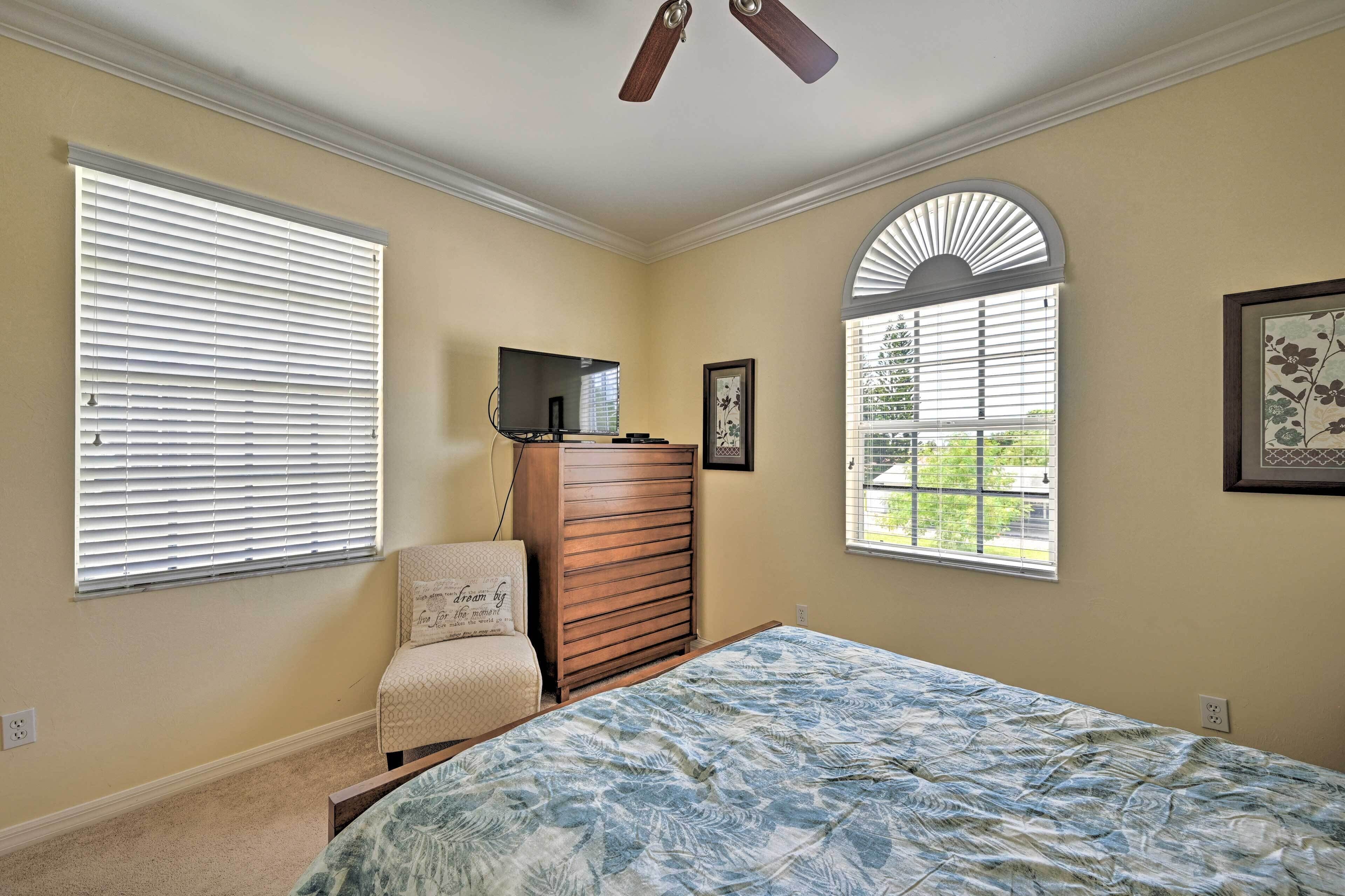 A bedroom with a bed, a dresser, a TV, and a window with blinds.