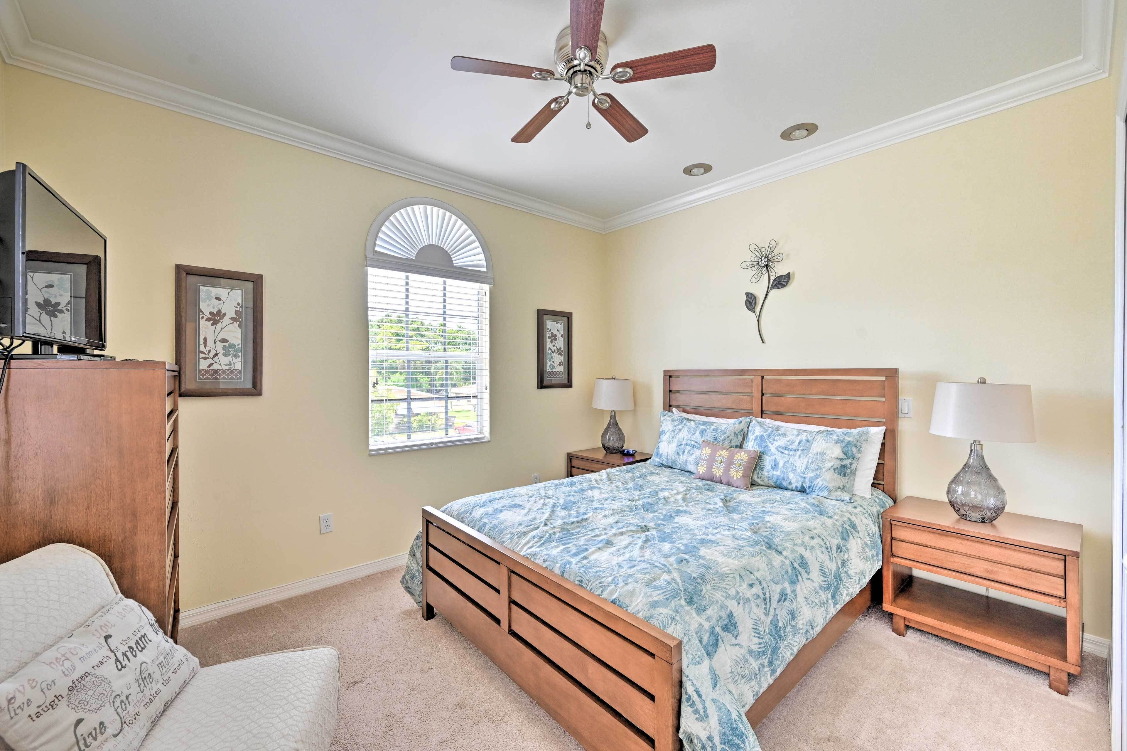 A bedroom with a bed, nightstands, a ceiling fan, a window, and wall art.