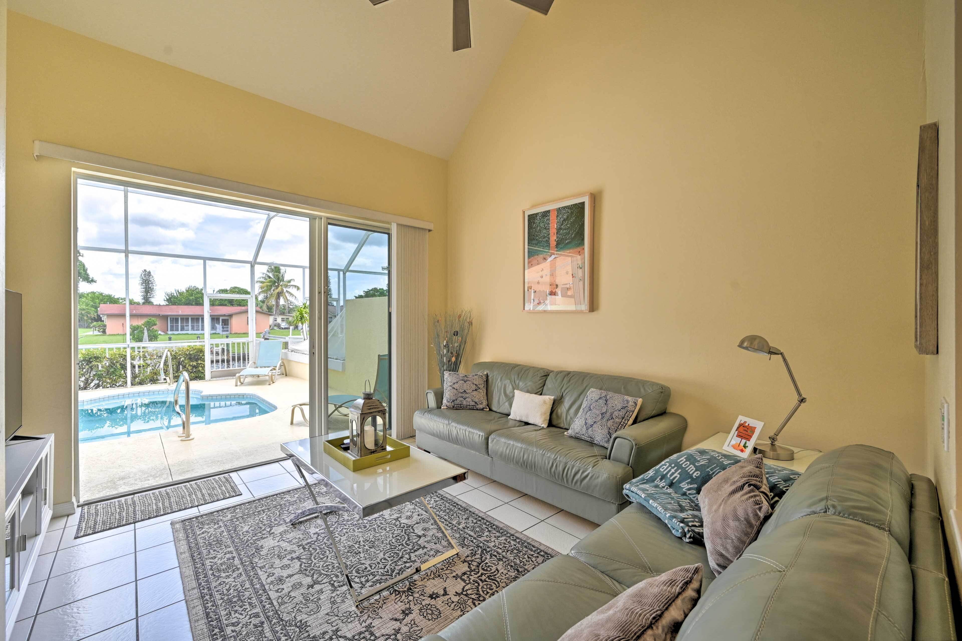 A living room with a green sofa, a coffee table, and a view of a swimming pool through a glass door.