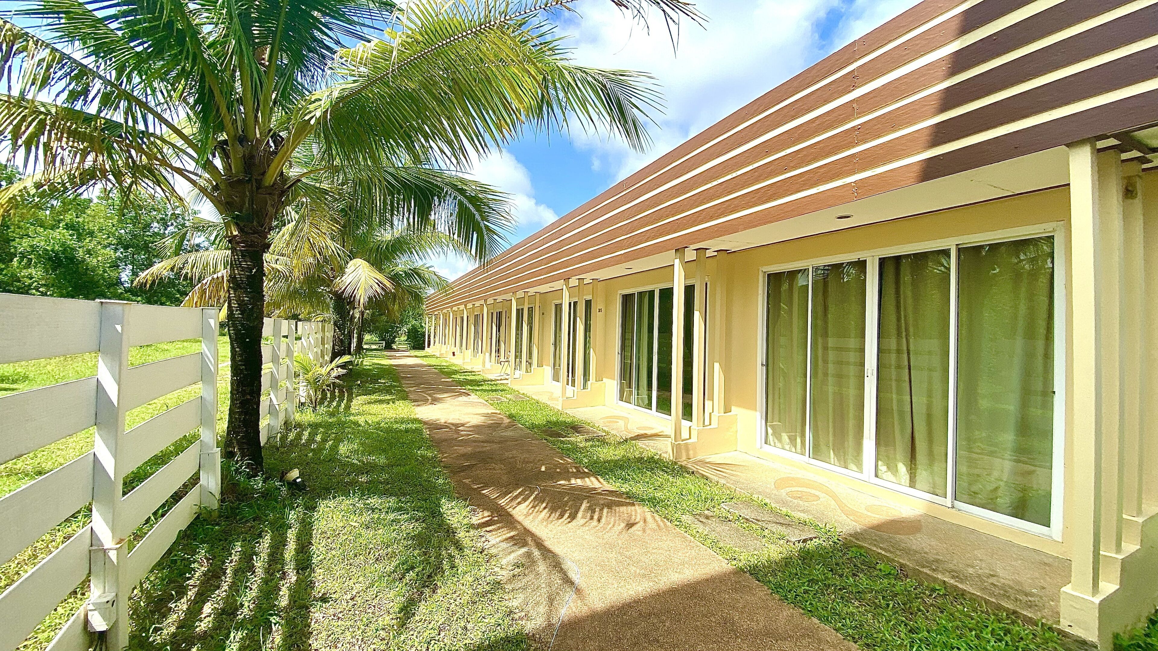 A row of hotel rooms with large sliding glass doors, a white fence, and palm trees.