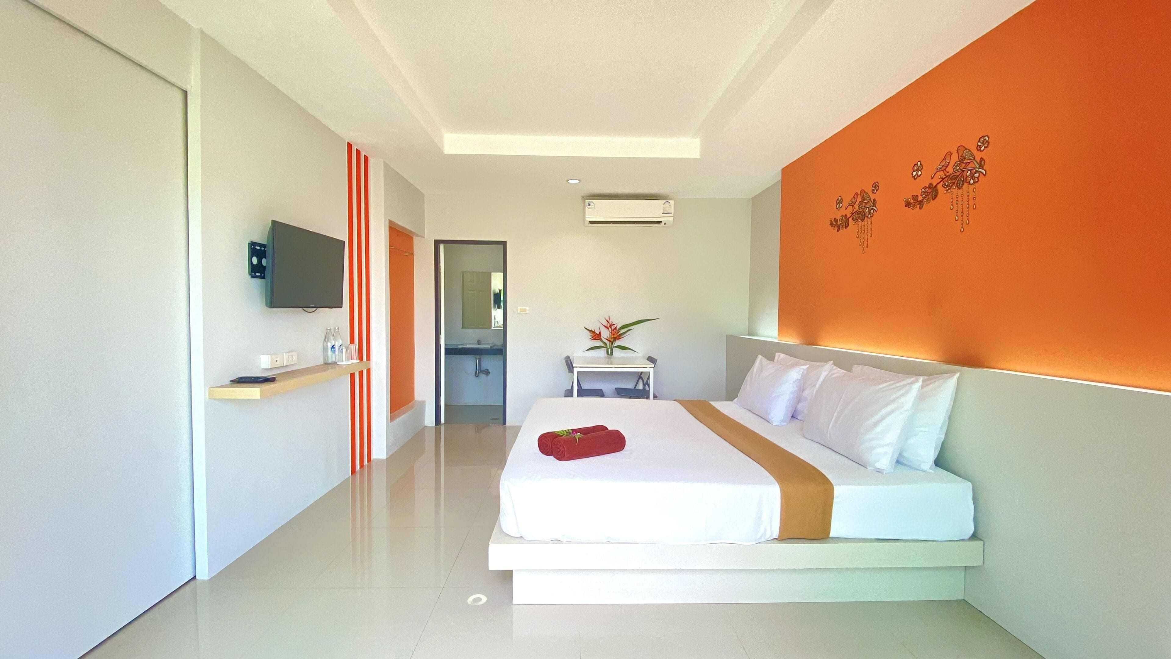 A modern hotel room with a large bed, a TV mounted on the wall, and a small table with a vase of flowers.
