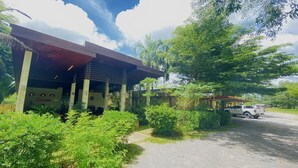 A building with a covered outdoor seating area, surrounded by lush greenery and a parked vehicle. - Kuapa Resort (Takua Pa)