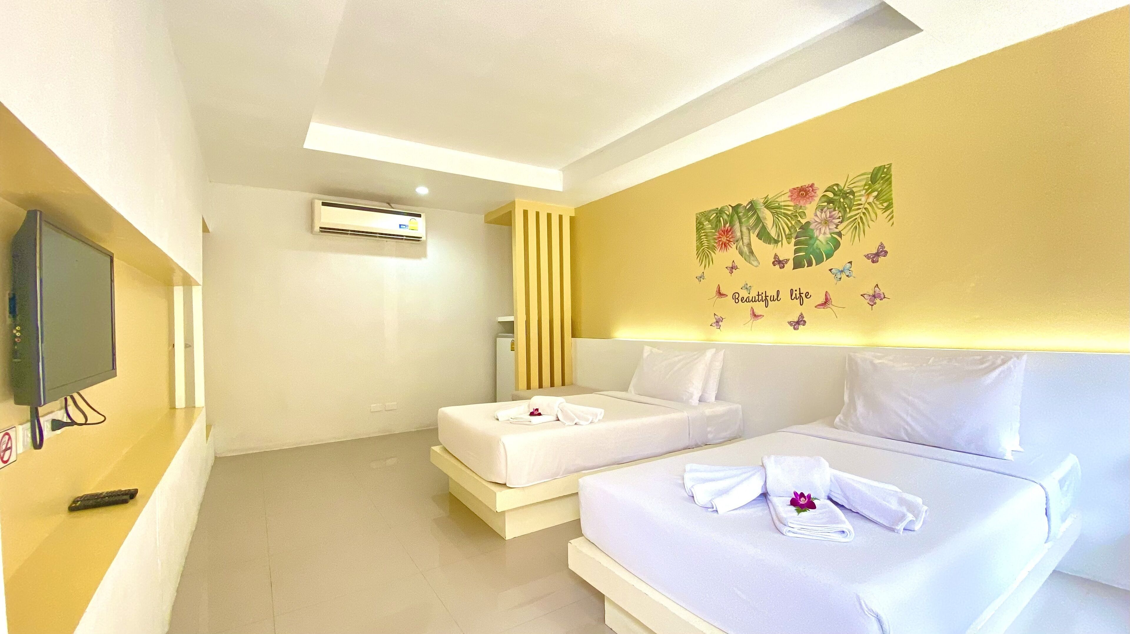 A hotel room with two beds, a TV, an air conditioning unit, and a wall decoration.