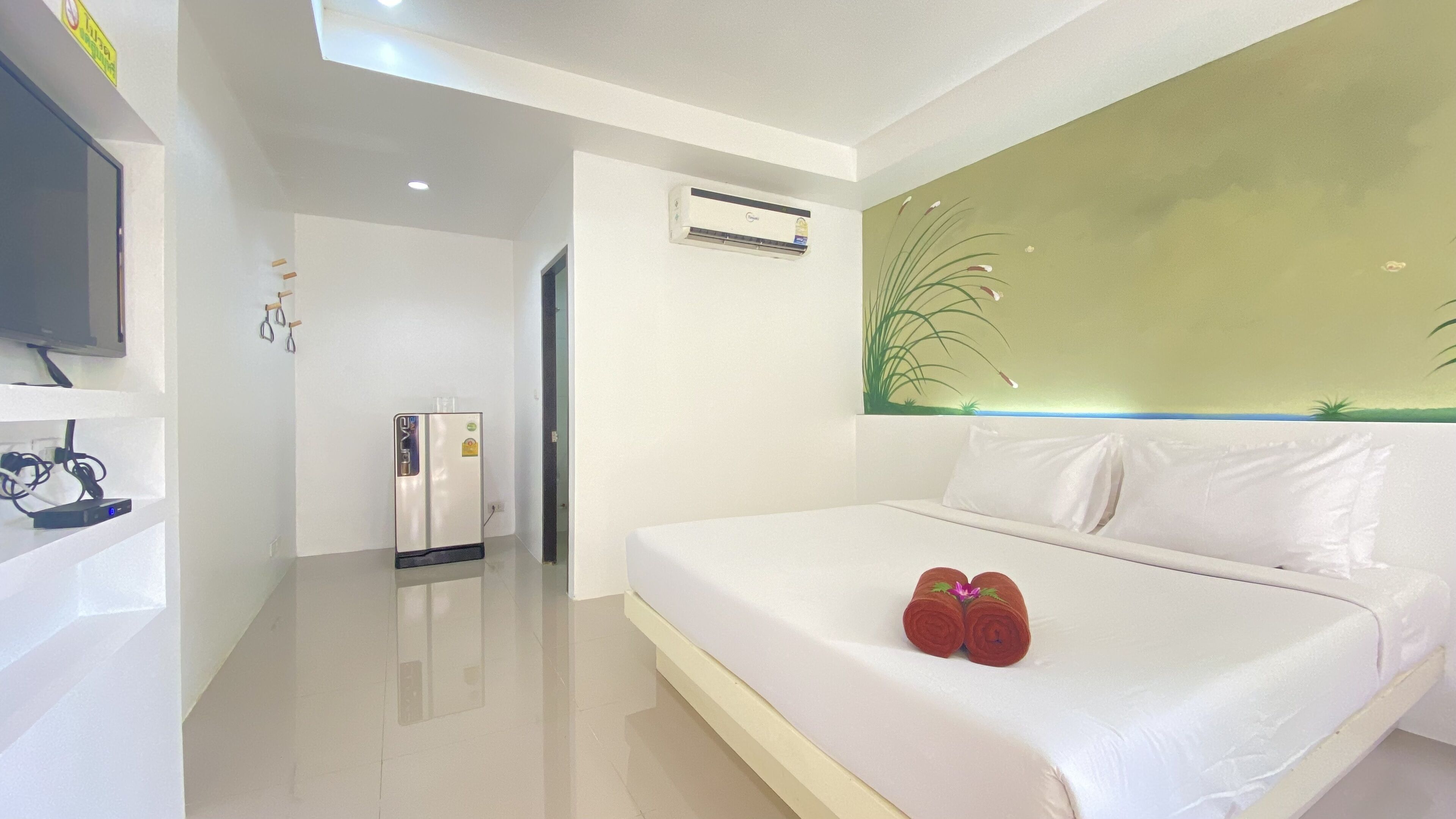A modern hotel room with a large bed, a flat-screen TV mounted on the wall, a built-in air conditioning unit, and a minimalist design.