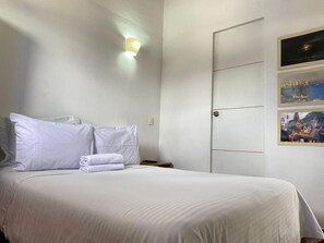 Un lit bien fait, avec du linge de lit blanc, une lampe fixée au mur et une porte au design simple.