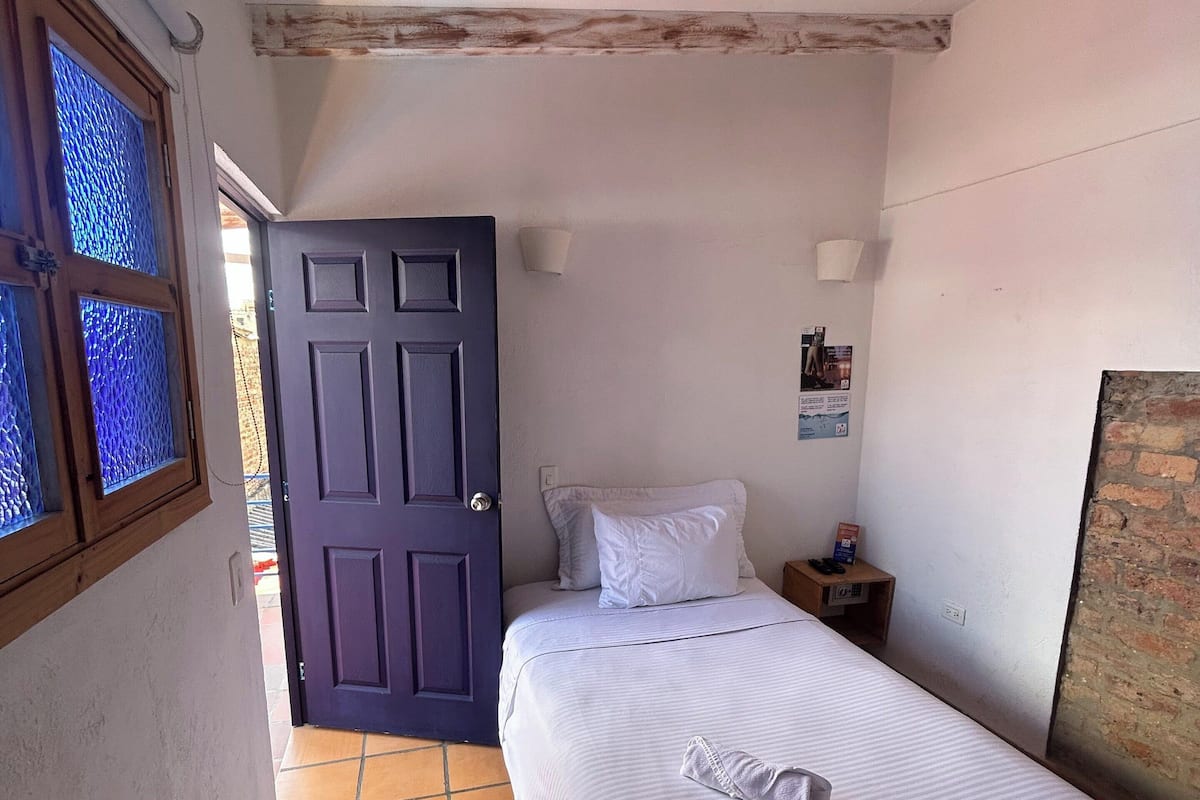 Un dormitorio con cama, mesita de noche, lámpara de pared y puerta que da a otra habitación.