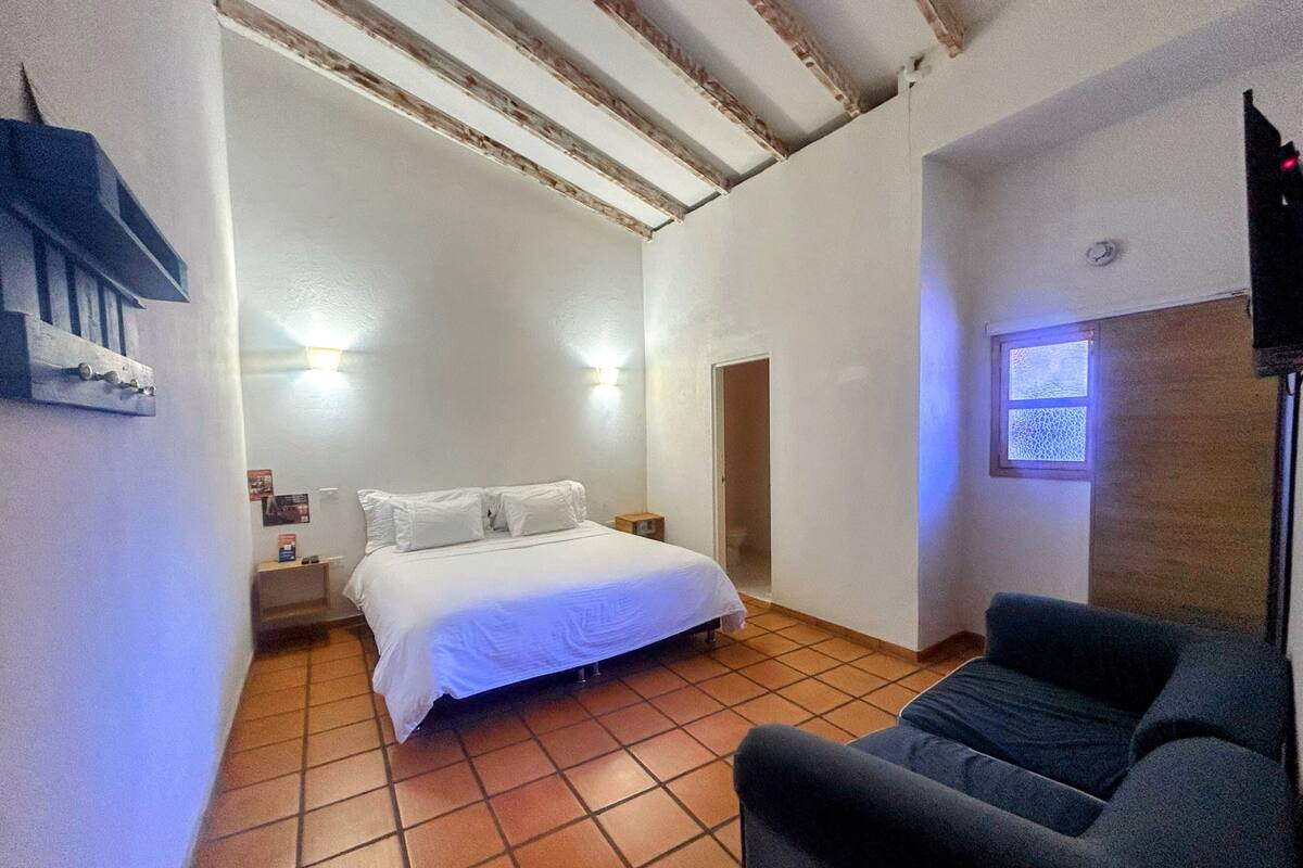 Una habitación pequeña y luminosa con una cama, una silla y una ventana.