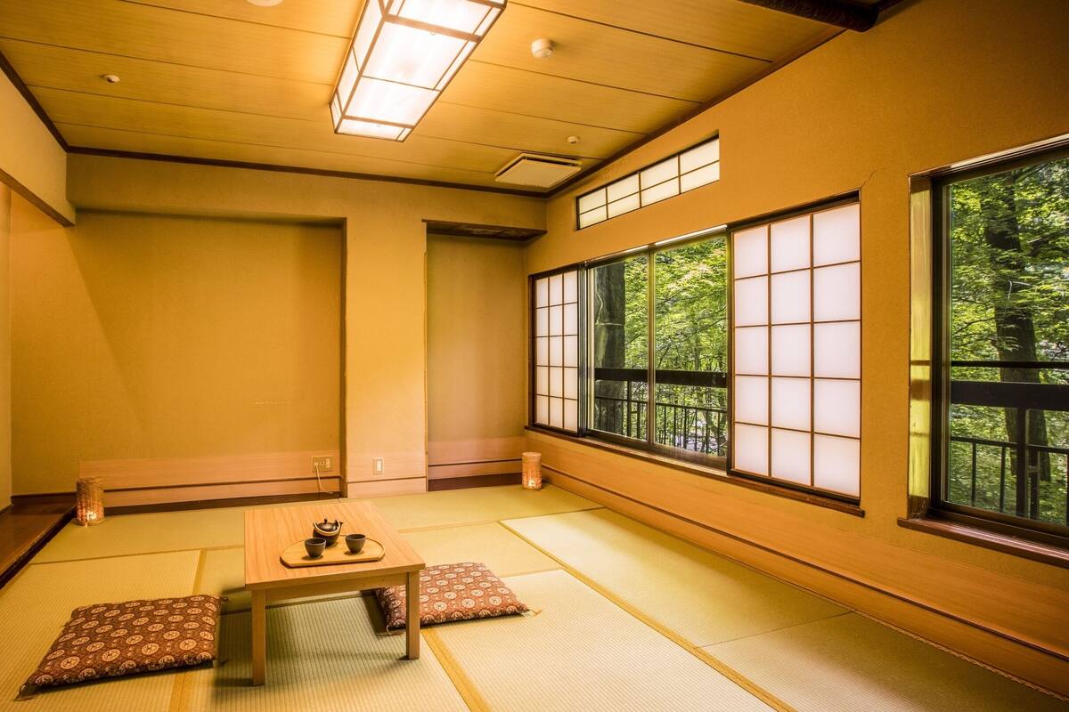 Une pièce de style japonais traditionnel, avec un sol recouvert de tatamis, une petite table sur laquelle sont disposés des ustensiles à thé, et de grandes fenêtres ornées de paravents en papier.