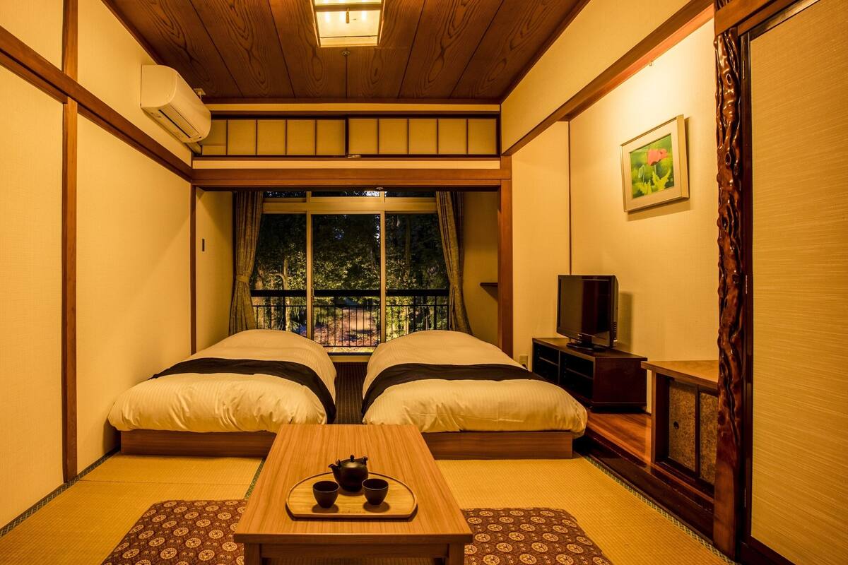 Une pièce de style japonais traditionnel, avec un sol recouvert de tatamis, un futon servant de lit, une petite table en bois accompagnée d’un service à thé et un téléviseur.