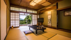 A traditional Japanese room with tatami flooring, a low table with a tea set, a television, and a view of a mountain through a sliding door. - Ooedo Onsen Monogatari Unazuki Grand Hotel (Kurobe)