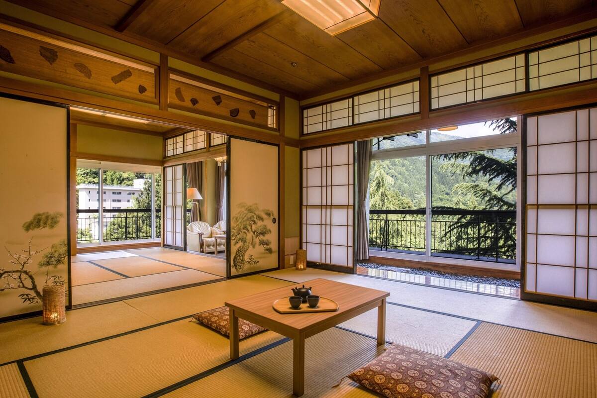 Une pièce de style japonais traditionnel, avec un sol recouvert de tatamis, des portes coulissantes et une vue sur un paysage montagneux.