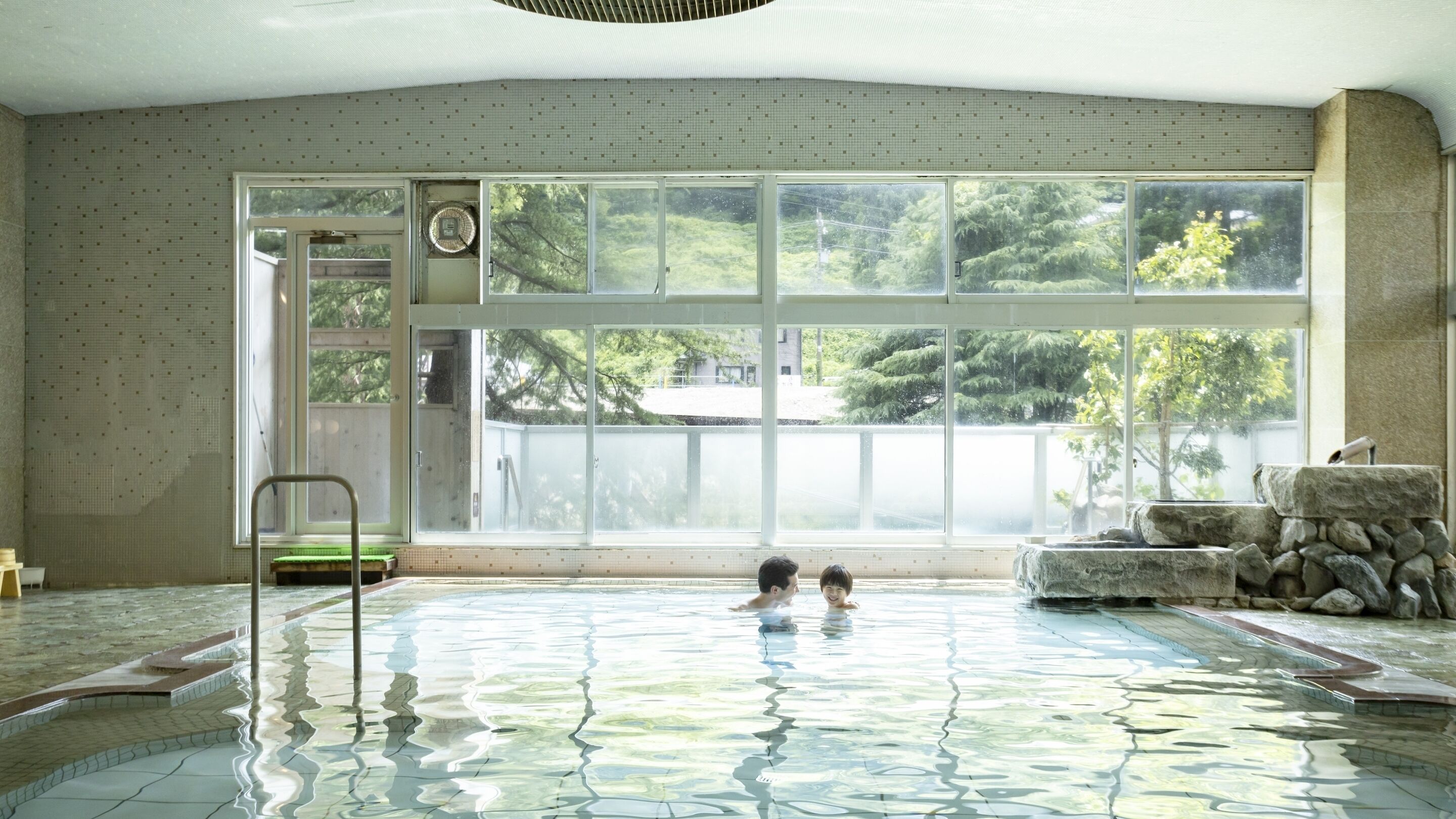An indoor swimming pool with a view of trees through large windows.