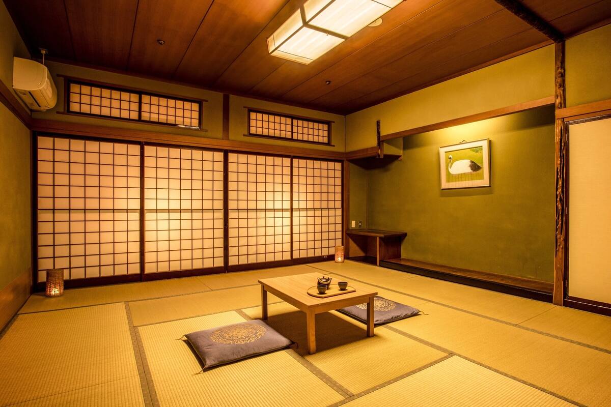 Une pièce de style japonais traditionnel, avec un sol recouvert de tatamis, des portes coulissantes, une petite table en bois et un tableau encadré accroché au mur.