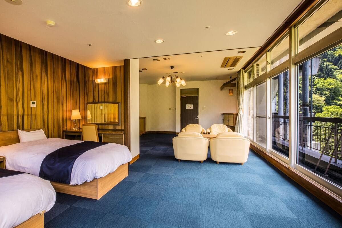 Une chambre d’hôtel avec deux lits, un coin salon et de grandes fenêtres donnant sur un paysage agréable.