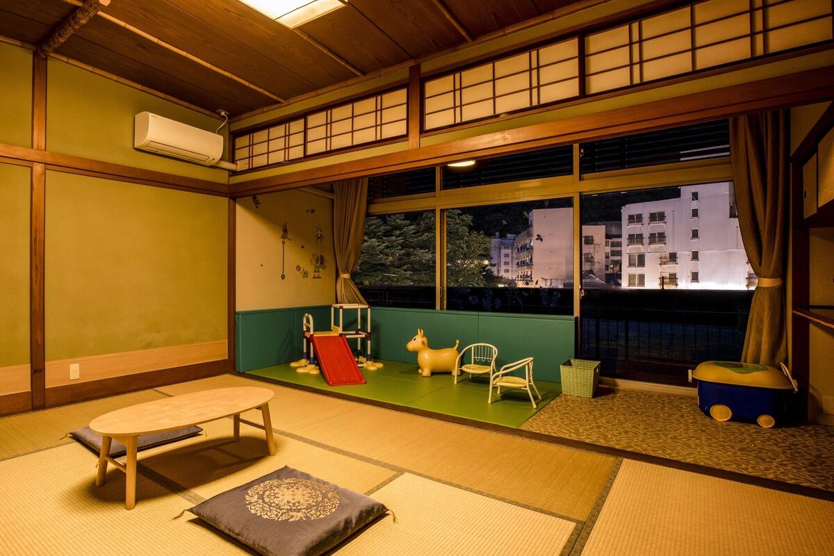 Une pièce de style japonais traditionnel, avec un sol recouvert de tatamis, un futon servant de lit, une petite table et une fenêtre donnant sur les bâtiments illuminés la nuit.
