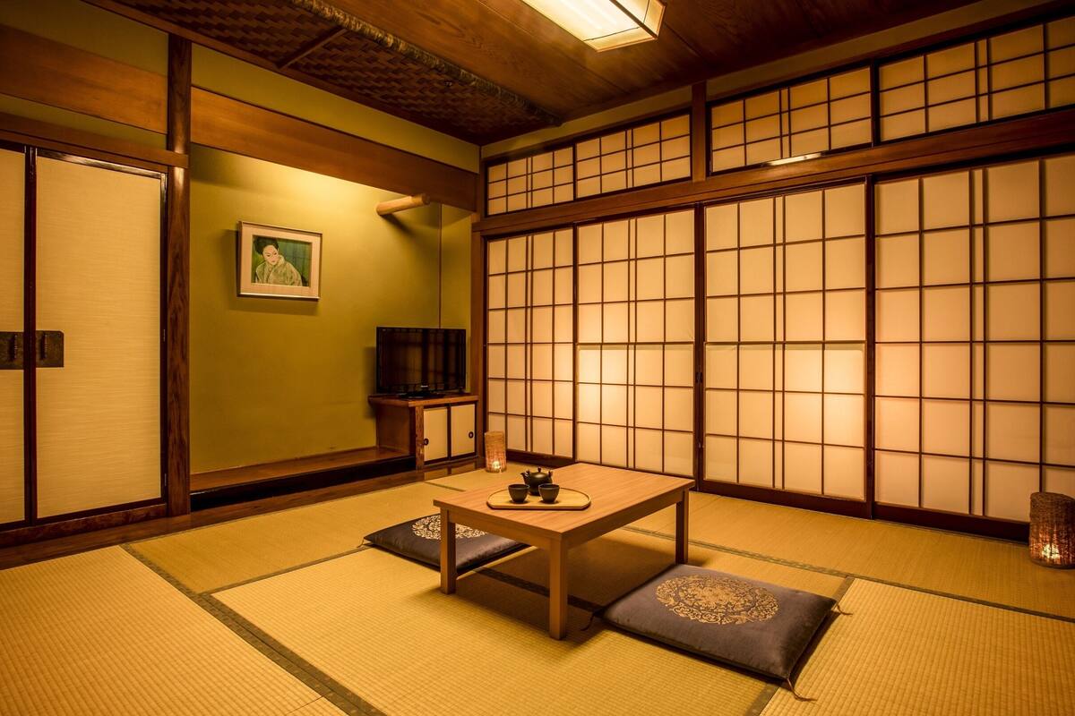 Une pièce de style japonais traditionnel, avec un sol recouvert de tatamis, une basse table en bois, des coussins, un téléviseur et des paravents en papier de riz (shoji).
