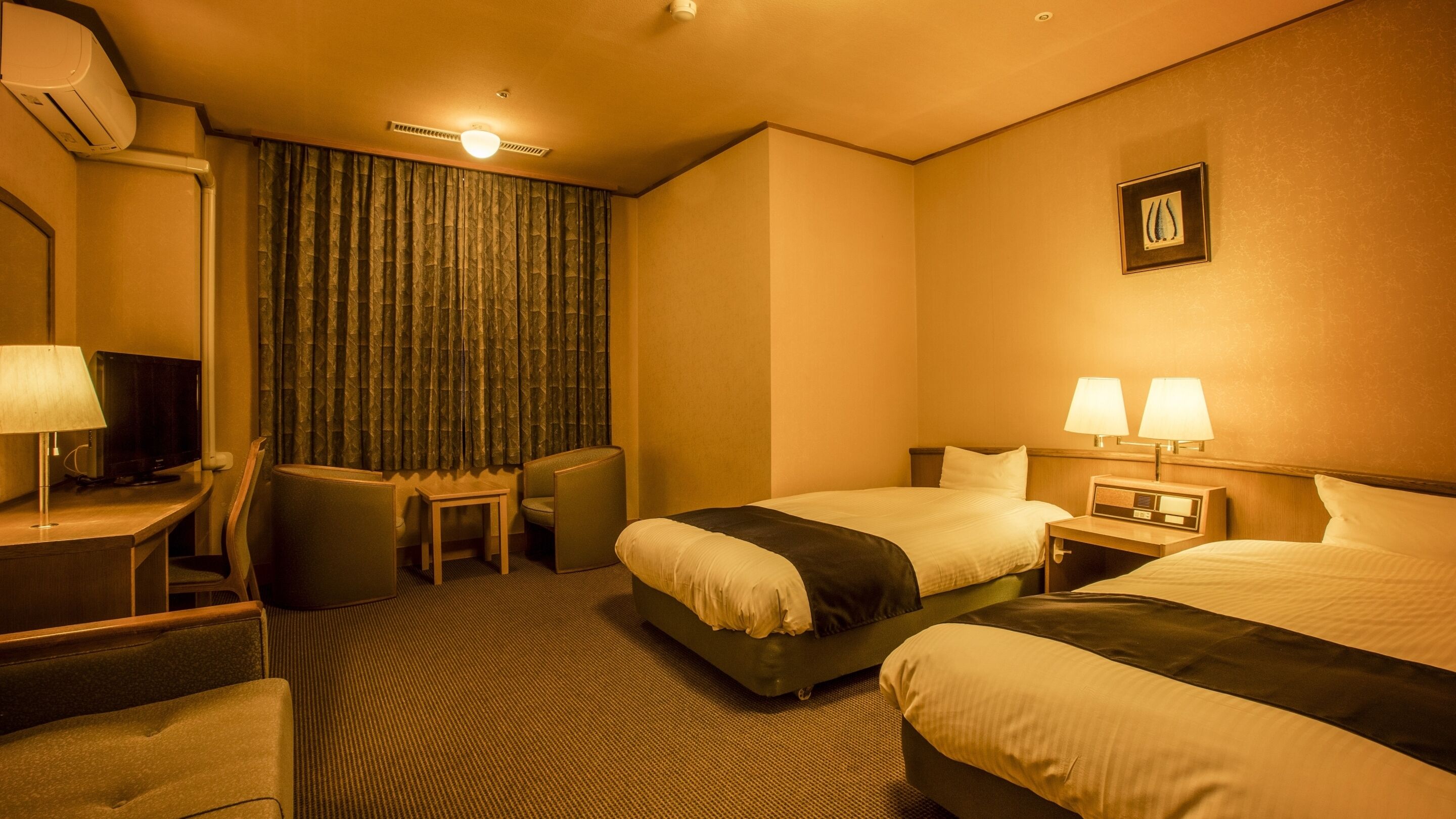 A hotel room with two beds, a desk with a lamp, a chair, a television, and a curtain.