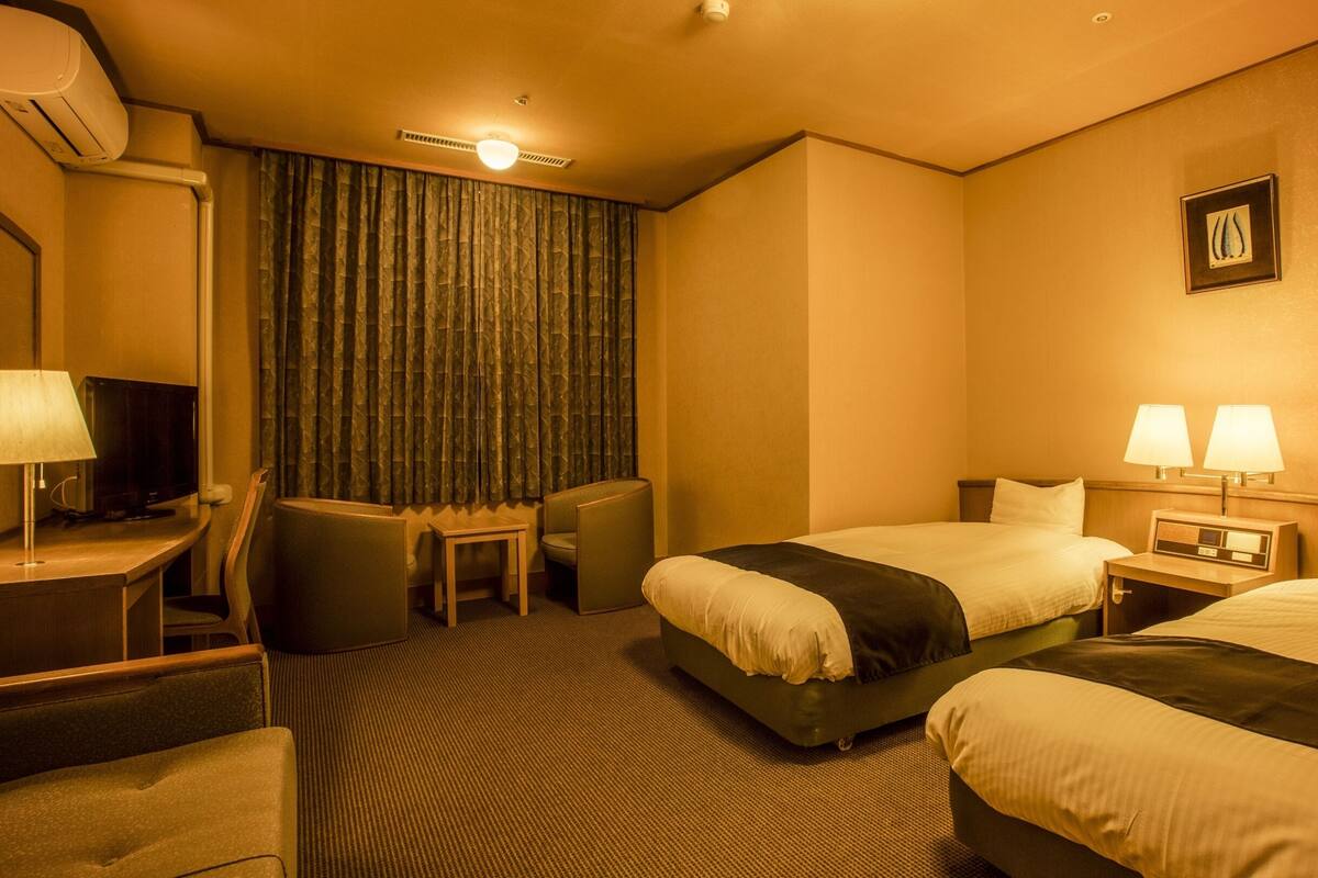 Une chambre d’hôtel avec deux lits, un bureau avec une lampe, une chaise, une télévision et un rideau.