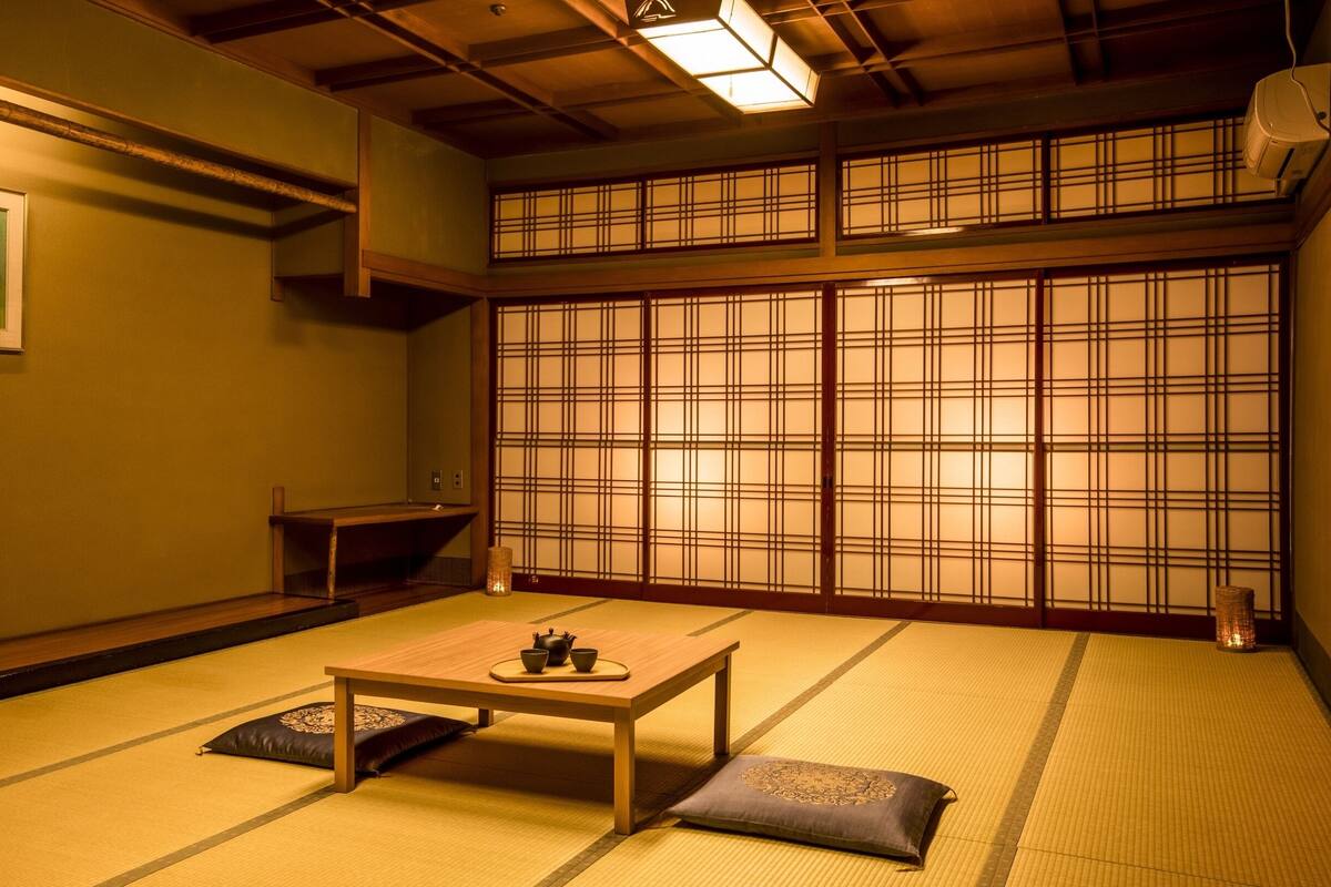 Une pièce de style japonais traditionnel, avec un sol recouvert de tatamis, une basse table en bois, des coussins et un paravent coulissant de type shoji.