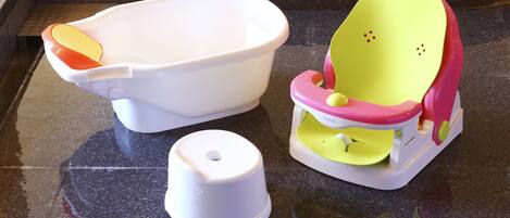 A kitchen counter with a white plastic basin, a yellow and pink high chair, and a white plastic container.