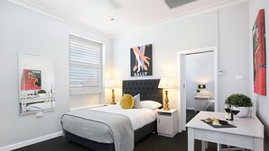 Ett modernt hotellrum med en stor säng, sängbord med lampor, ett litet skrivbord och konstverk på väggarna.