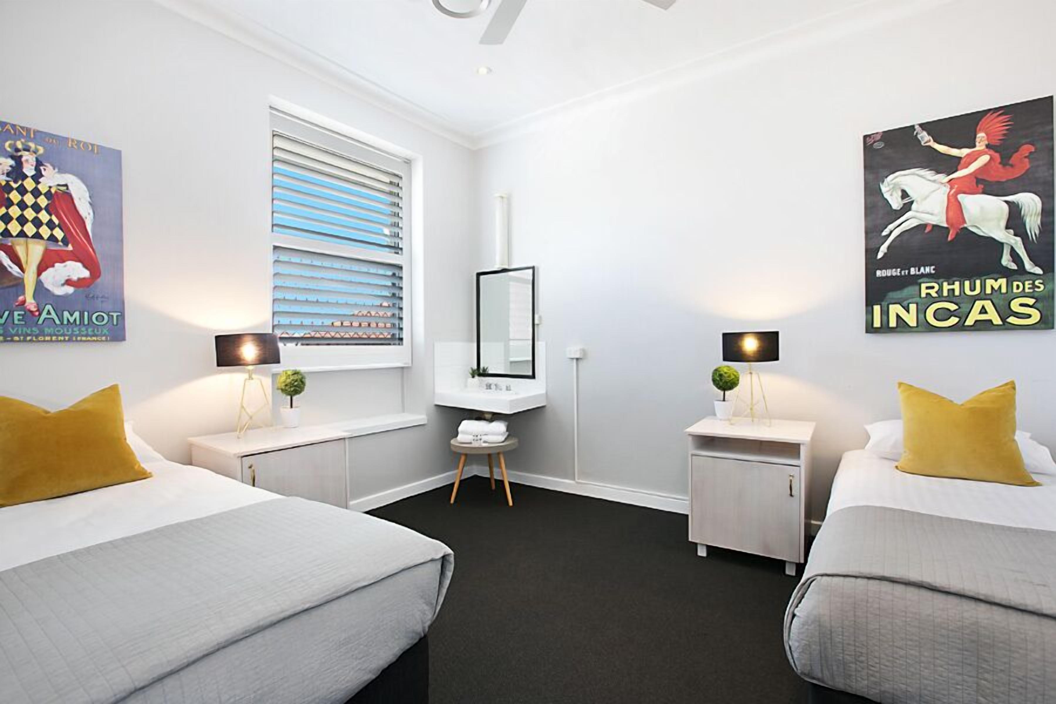 A hotel room with two beds, a small desk, a mirror, and artwork on the walls.