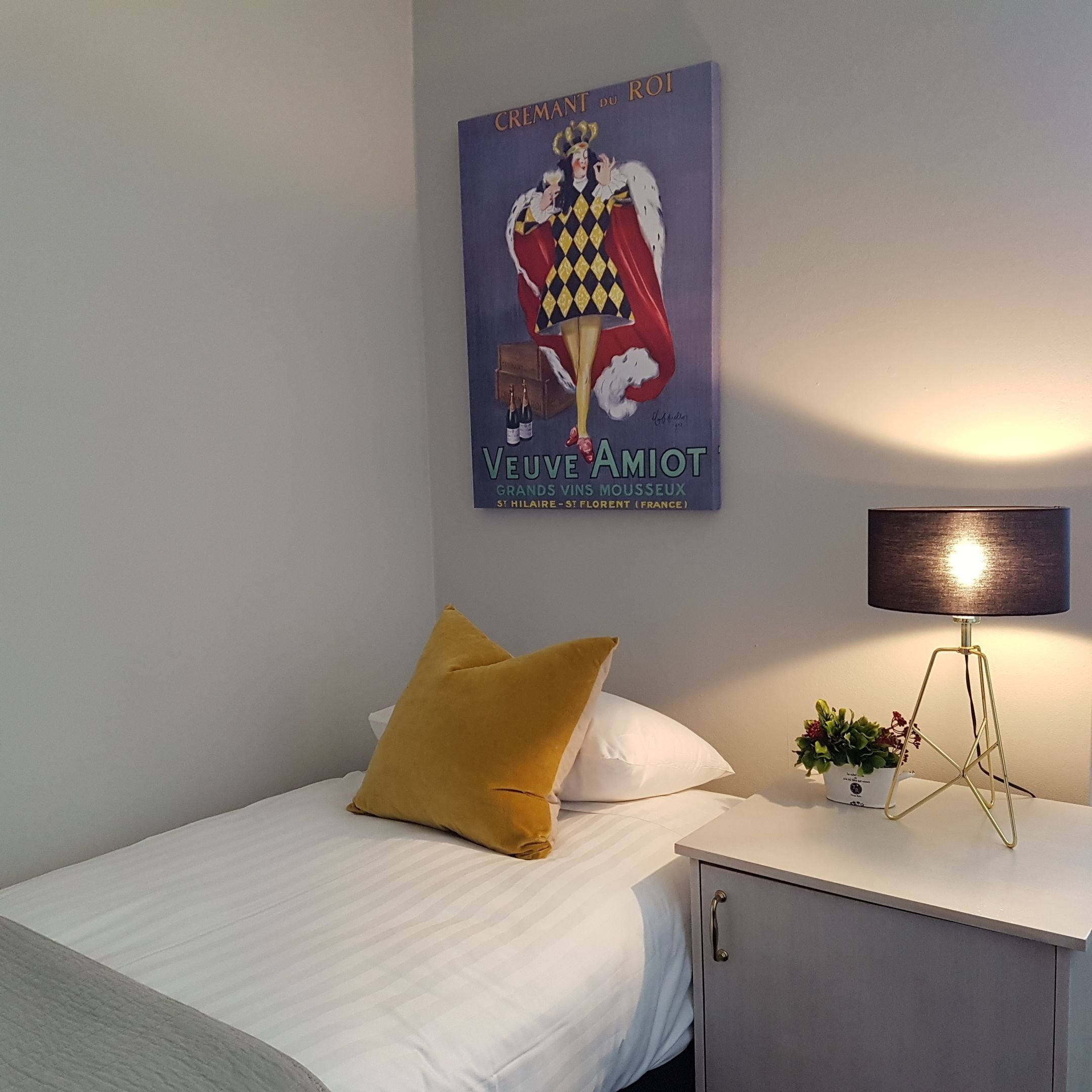 A bedroom with a bed, a nightstand, a lamp, and a poster on the wall.