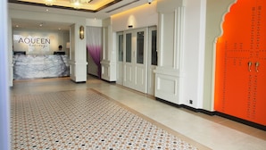 Zona de recepción de hotel con mostrador de mármol, alfombra estampada y una puerta naranja llamativa.
