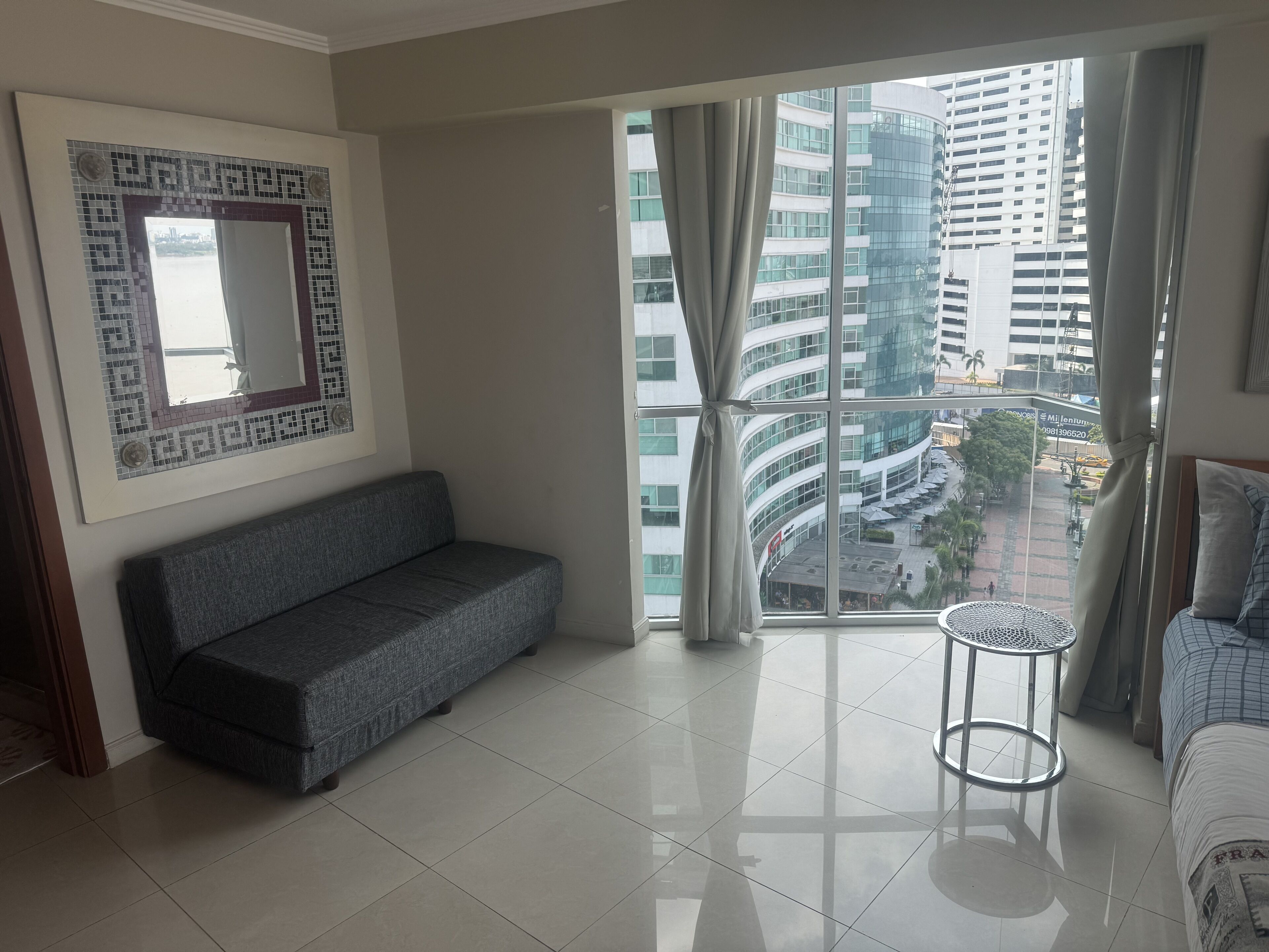Una sala de estar moderna con un sofá gris, una mesita redonda y un ventanal con cortinas.