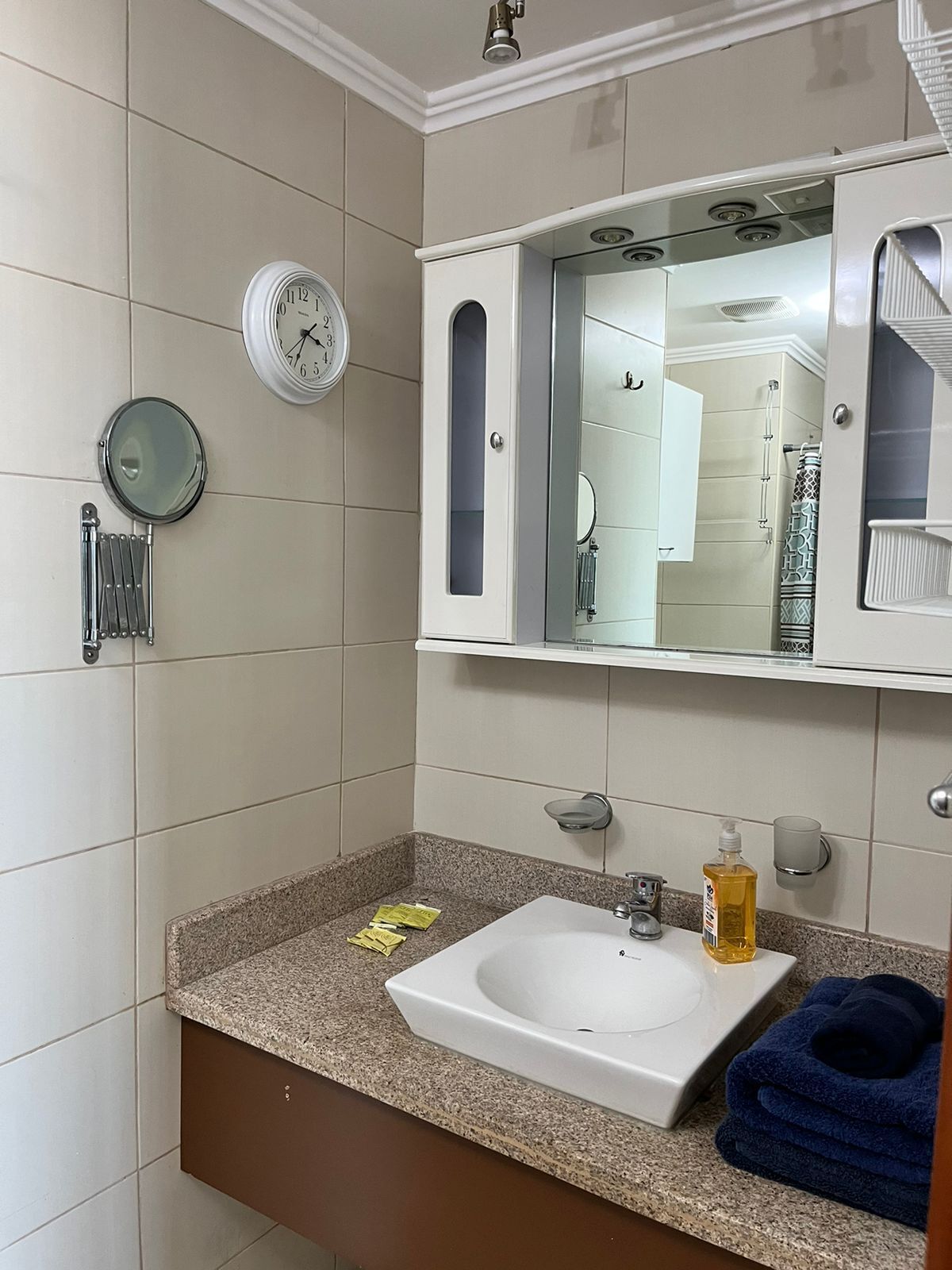 A bathroom with a white sink, a mirror, a clock, and a towel rack.