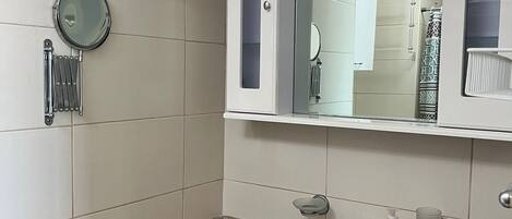 A bathroom with a white sink, a mirror, a clock, and a towel rack.