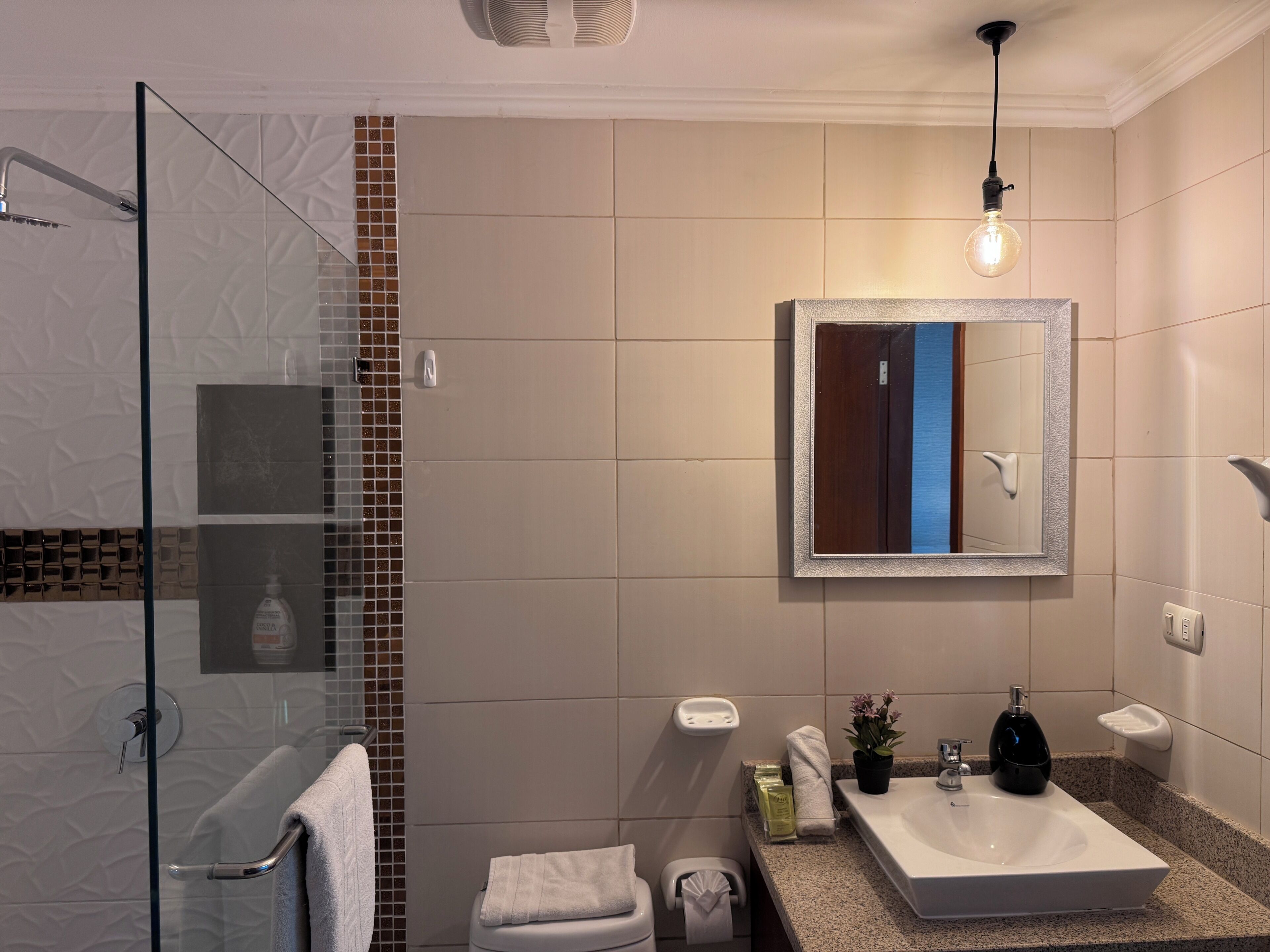 Un baño moderno con cabina de ducha de vidrio, un lavamanos blanco con espejo y un perchero para toallas.