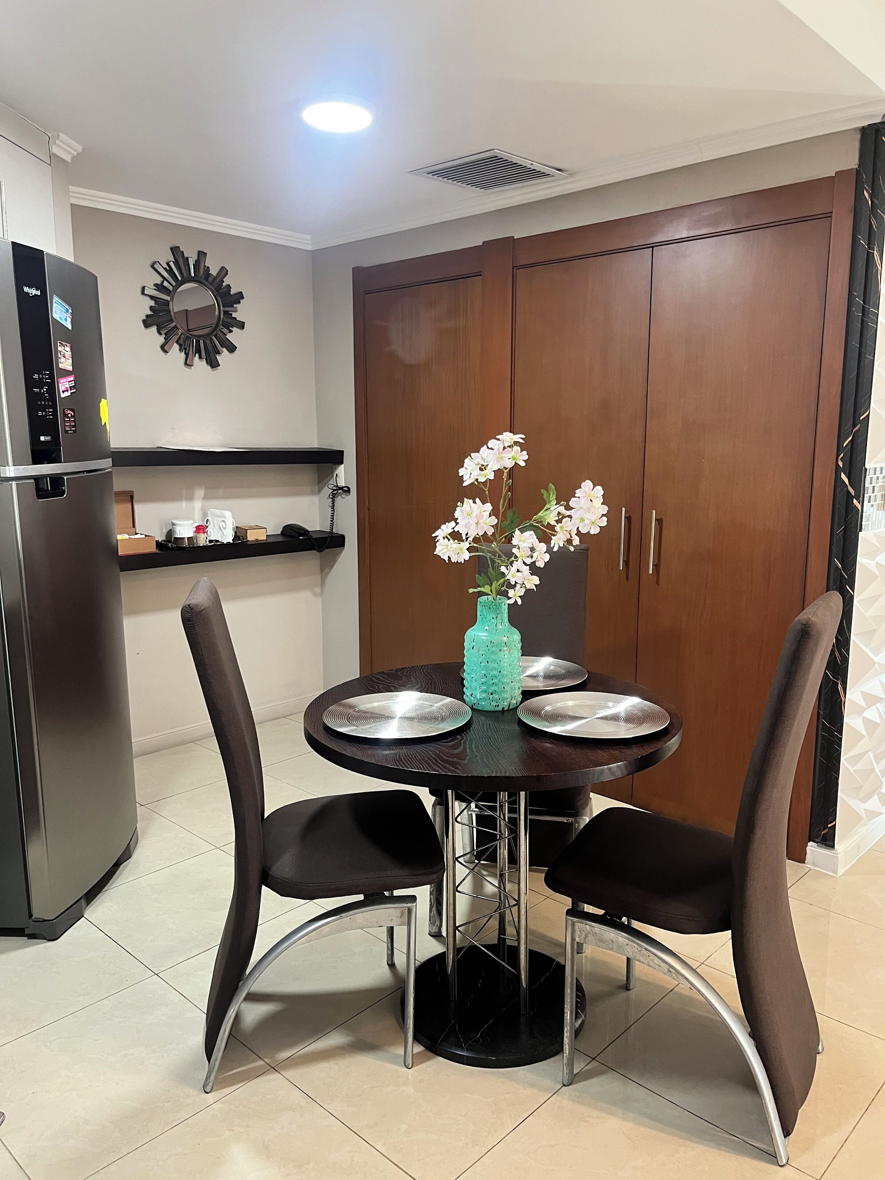 Une cuisine compacte comprenant une table à manger, des chaises, un réfrigérateur et un vase décoratif.