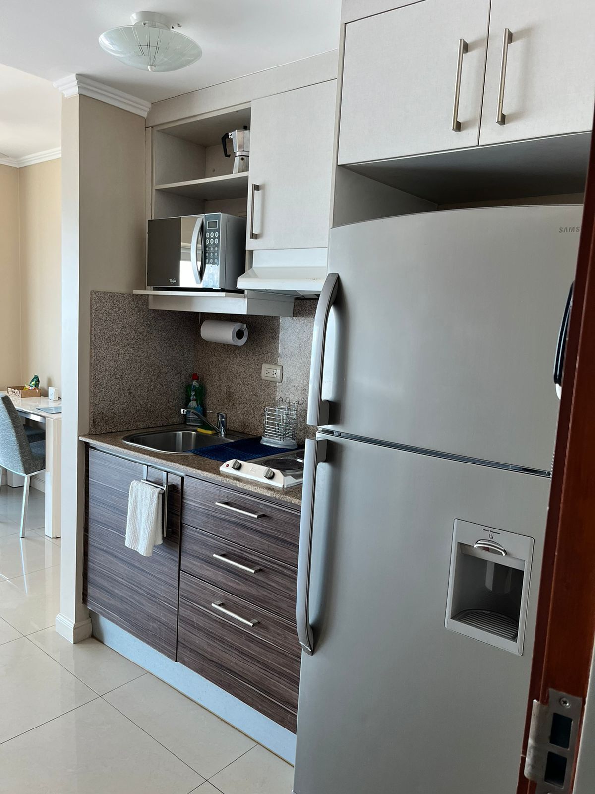 Una cocina moderna con microondas integrado, refrigerador de acero inoxidable y encimera con pileta.
