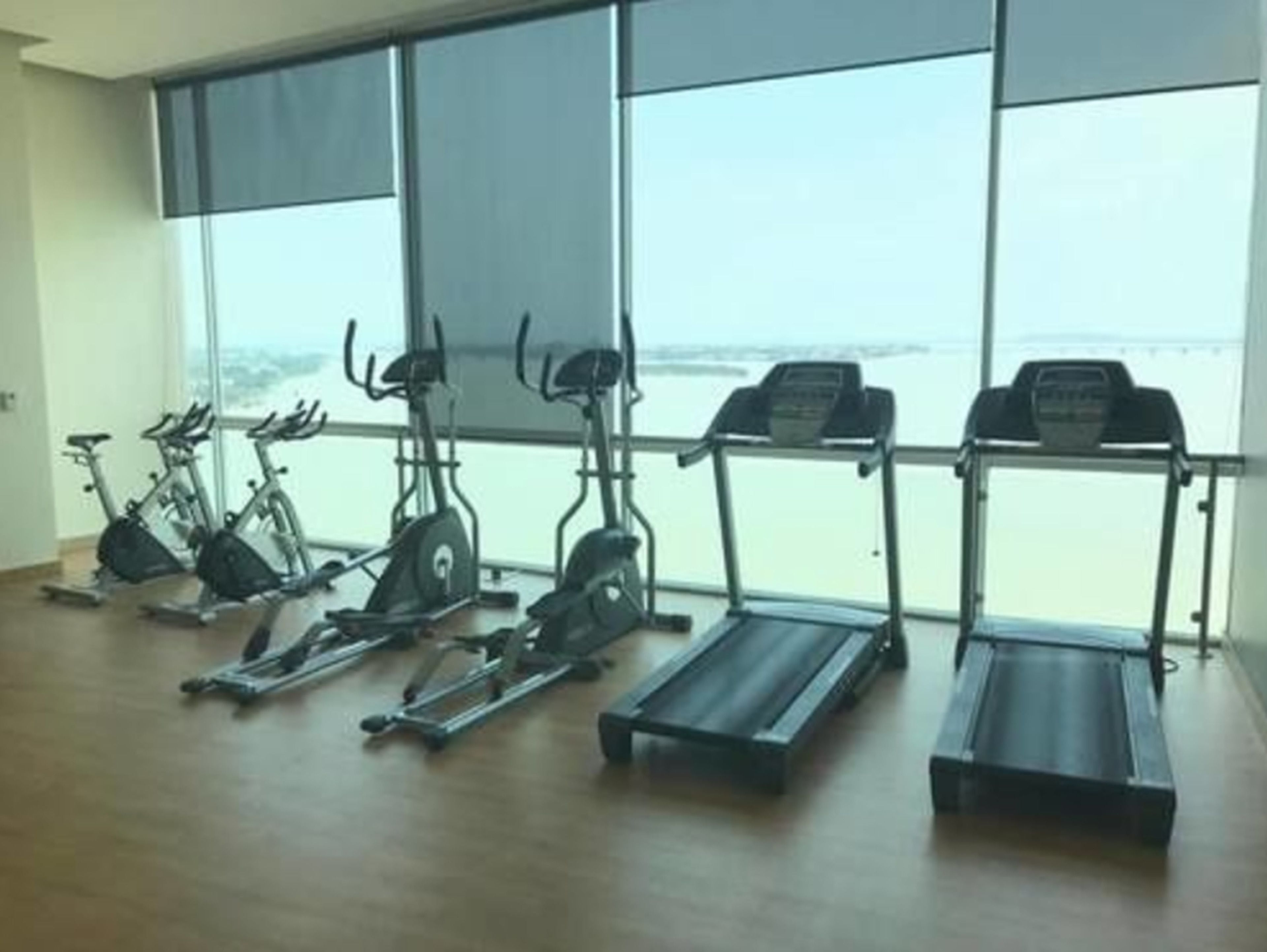 Un gimnasio con bicicletas estáticas, elípticas y cintas de correr, con amplios ventanales que ofrecen vista al mar.