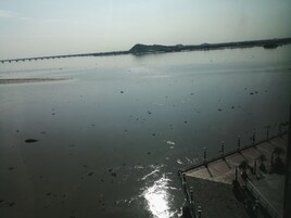 A calm body of water with a distant landmass, a bridge, and a paved walkway with lampposts.