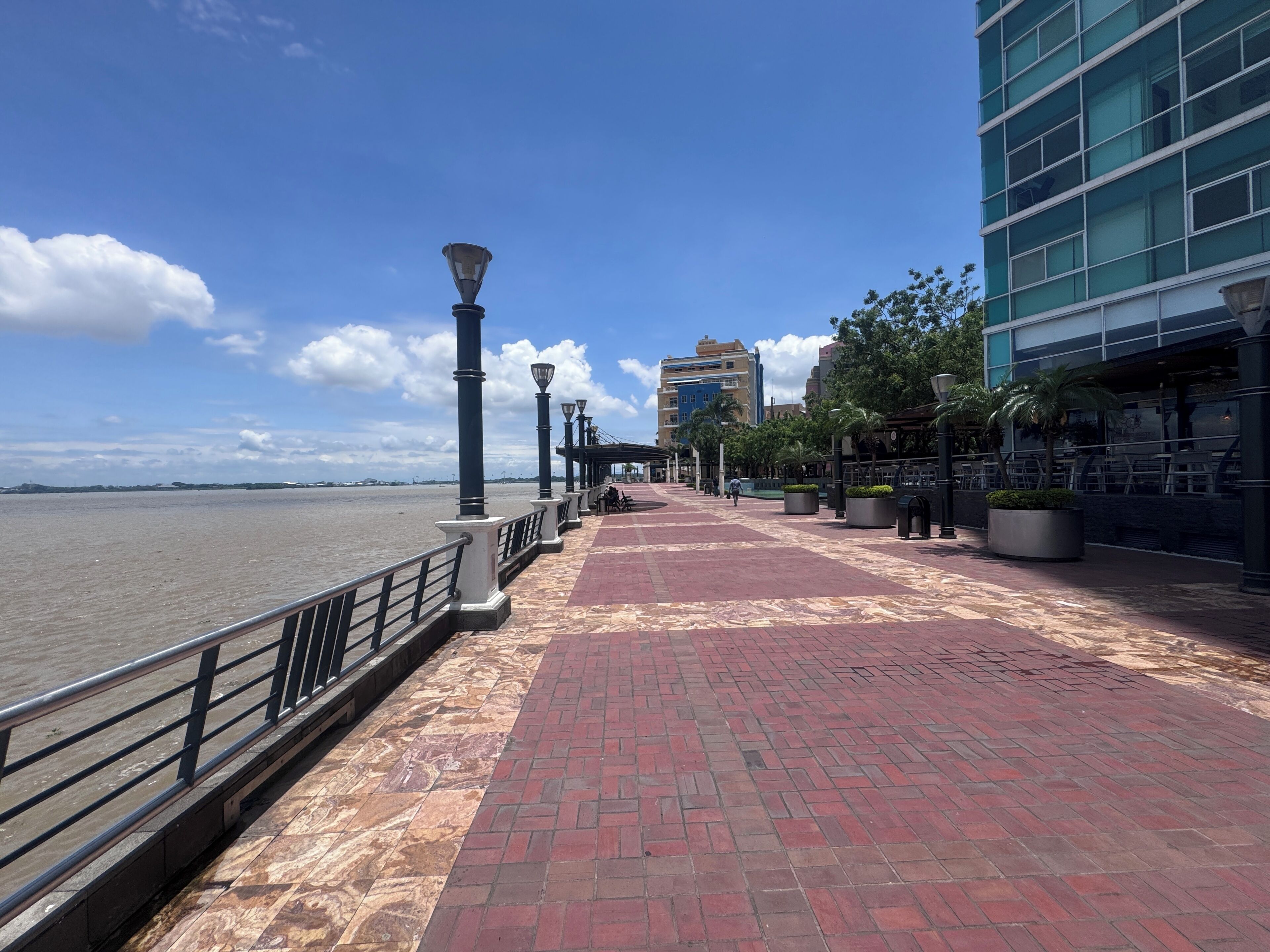 Une promenade en bord de mer, avec un chemin pavé de briques, des lampadaires et un bâtiment moderne doté de grandes fenêtres.