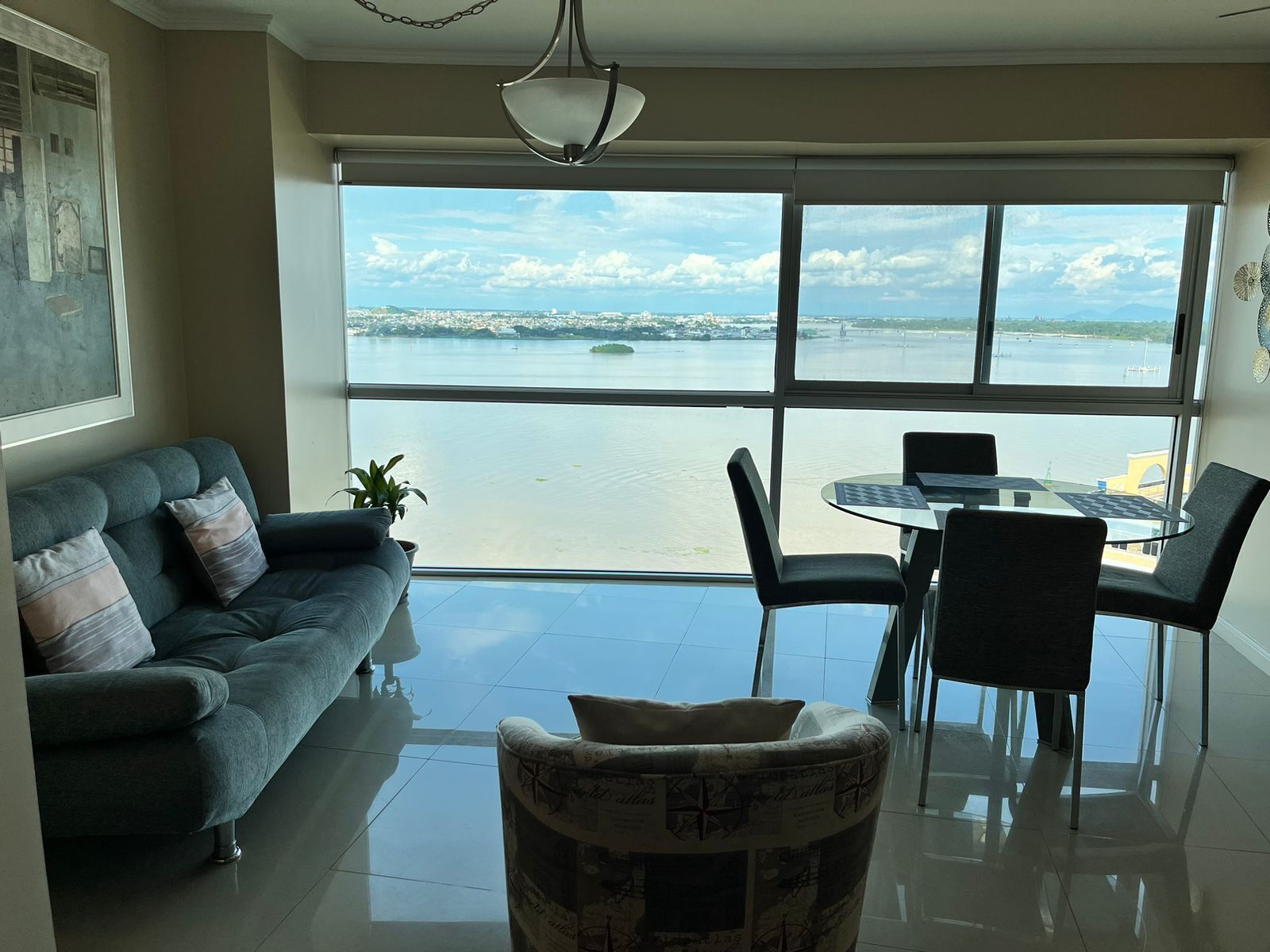 A modern living room with a large window, a sofa, a dining table with chairs, and a decorative chair.